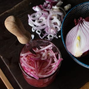 a fork sitting in a jar of sliced pickled onions next to a raw onion